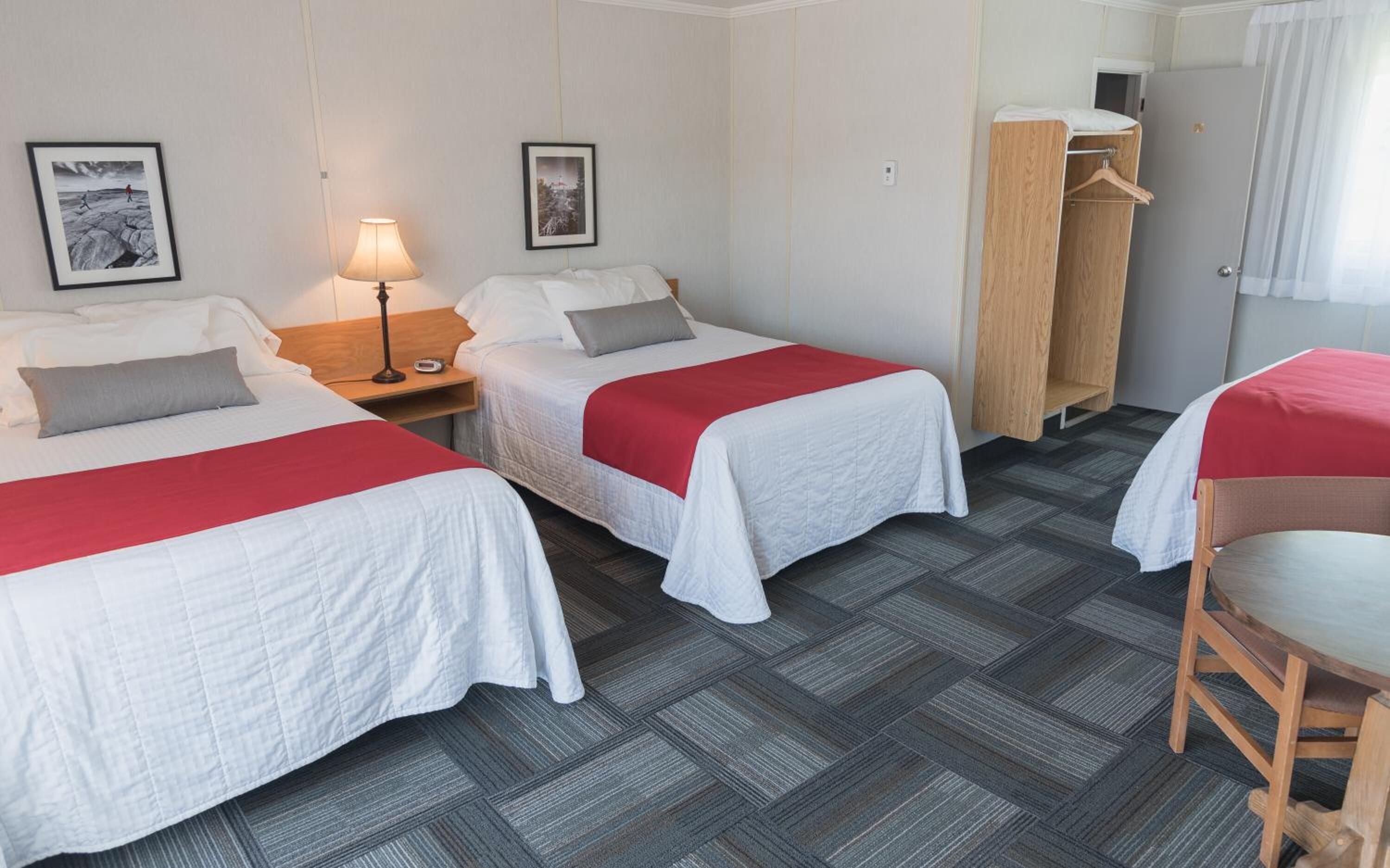 A hotel room with two beds, a nightstand with a lamp, a wooden wardrobe, and a chair.