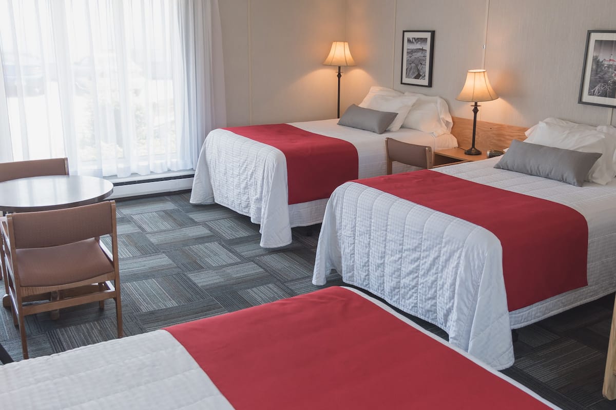 A hotel room with two beds, a dining table, and two lamps.