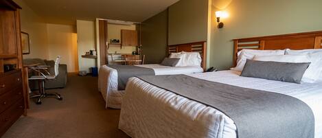 A hotel room with two beds, a desk, and a kitchenette.