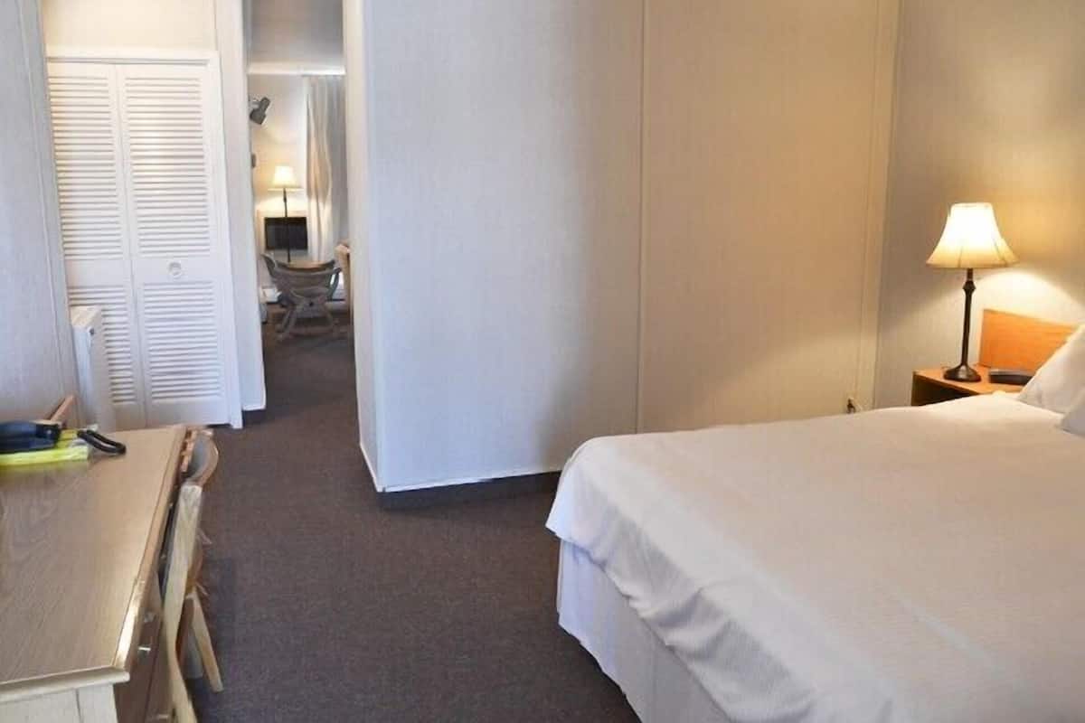A hotel room with a bed, a desk, and a chair. There is a lamp on the desk and a lamp on the nightstand.