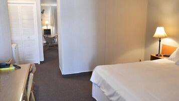 Een hotelkamer met een bed, een bureau en een stoel. Er staat een lamp op het bureau en een lampje op het nachtkastje.