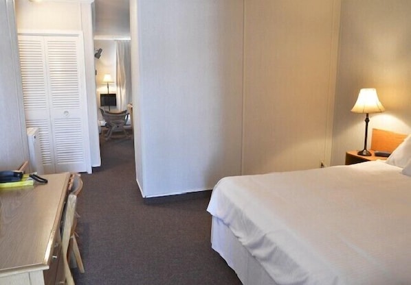 Una habitación de hotel con una cama, un escritorio y una silla. Hay una lámpara en el escritorio y otra en la mesita de noche.