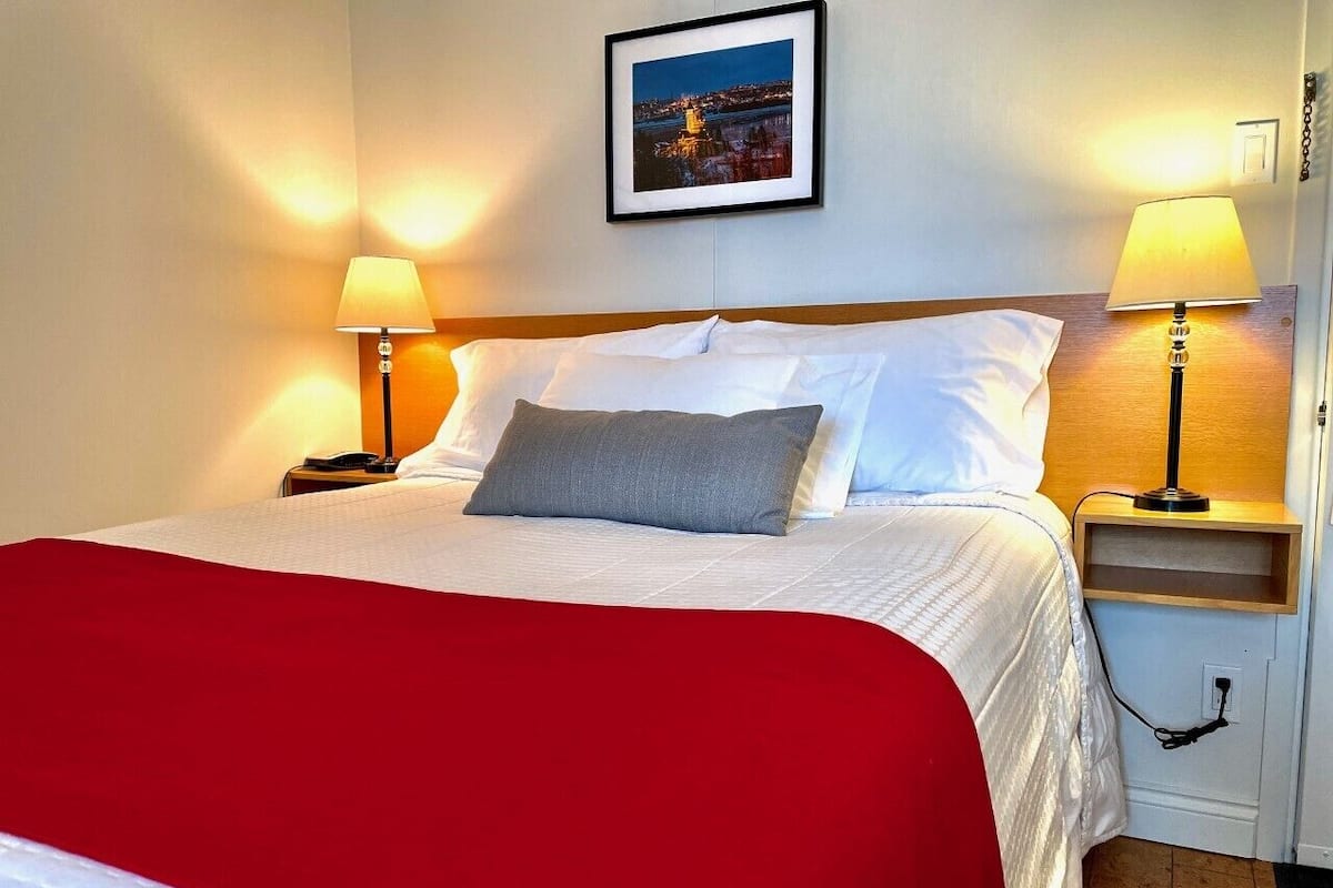A neatly made bed with a red blanket, two bedside lamps, and a framed picture on the wall.