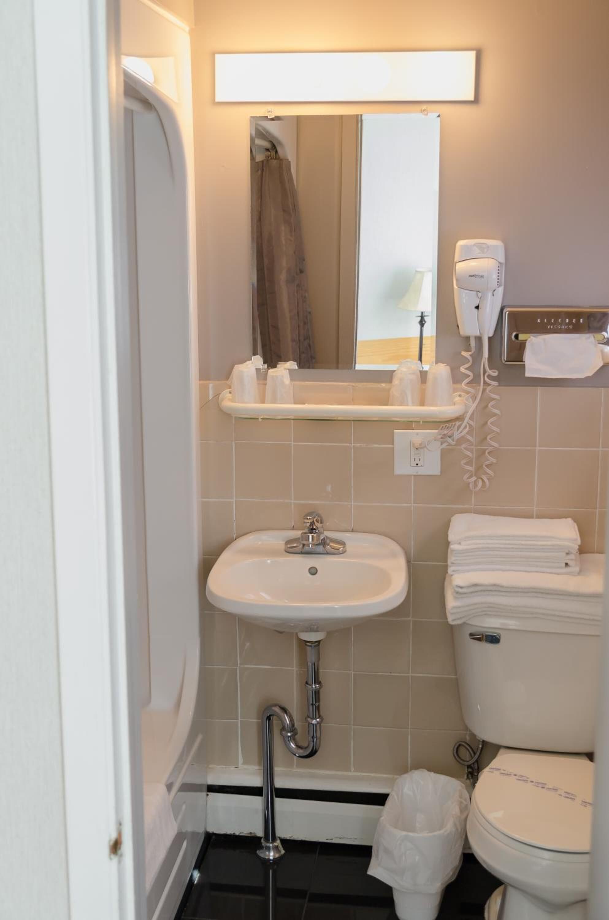 A bathroom with a sink, toilet, and a mirror. There is a towel rack with towels and a hairdryer on the wall.