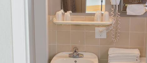 A bathroom with a sink, toilet, and a mirror. There is a towel rack with towels and a hairdryer on the wall.