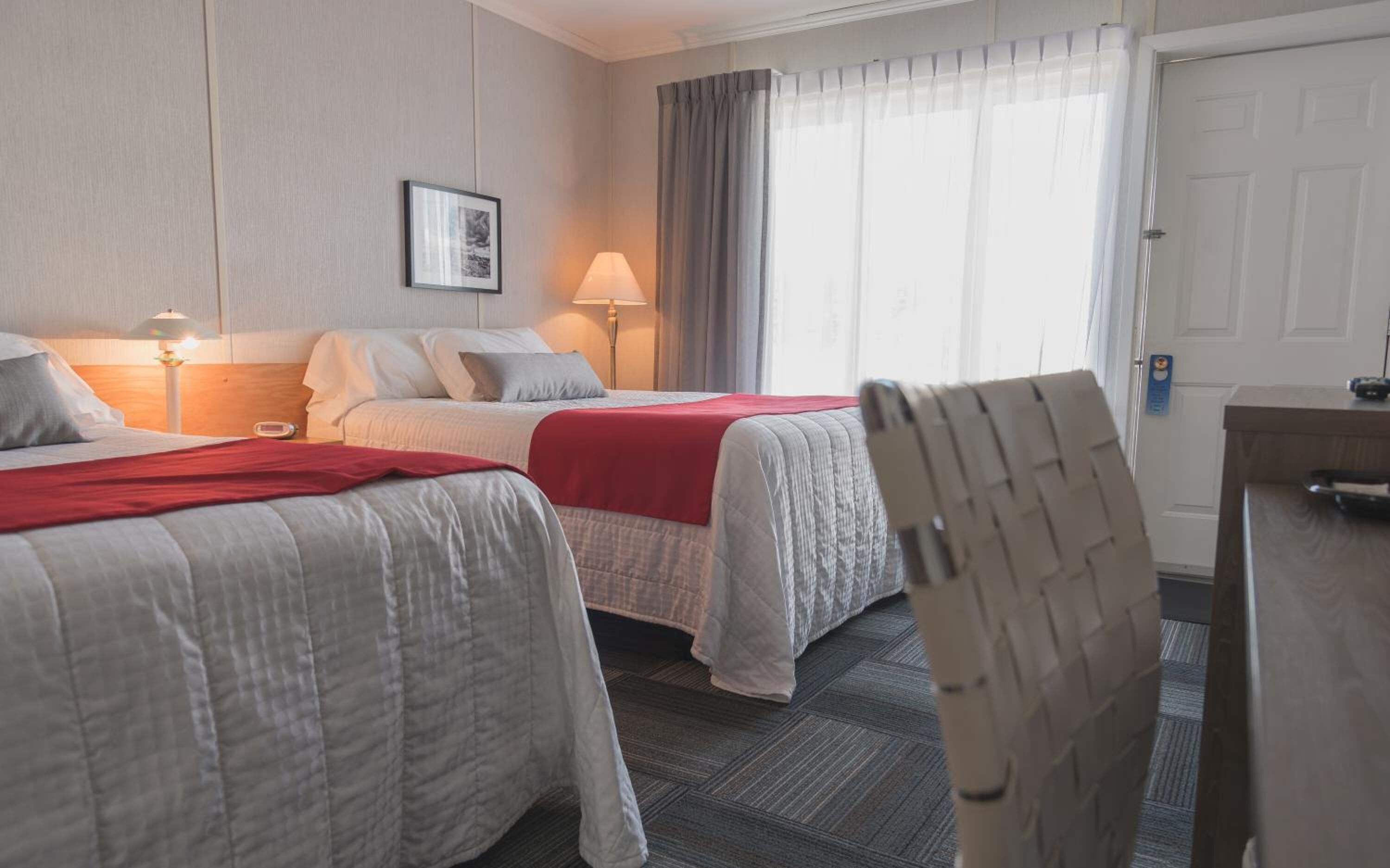 A hotel room with two beds, a desk, and a chair.