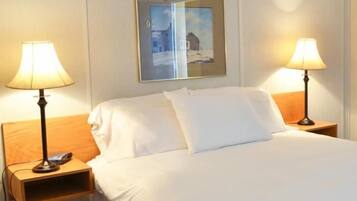 A neatly made bed with white linens, two bedside lamps, a nightstand with a phone, and a mirror reflecting a snowy landscape.