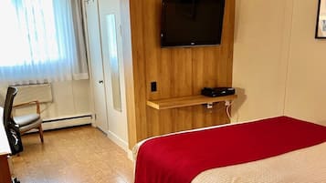 Habitación de hotel con cama, televisor montado en una pared de paneles de madera, una silla y un radiador.