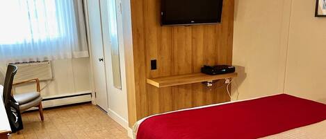 Ein Hotelzimmer mit Bett, Fernseher an einer Wand aus Holzpaneelen, einem Sessel und einer Heizung.