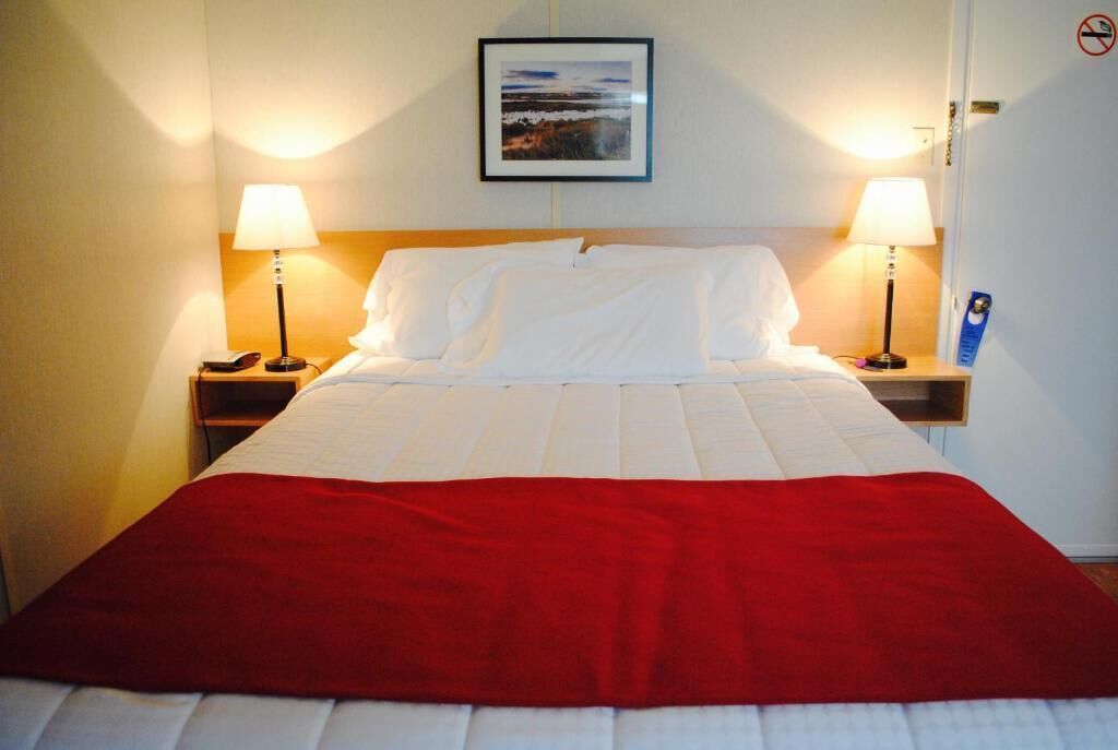 Une chambre d’hôtel avec un lit, deux lampes de chevet, un tableau encadré au mur et une couverture rouge sur le lit.