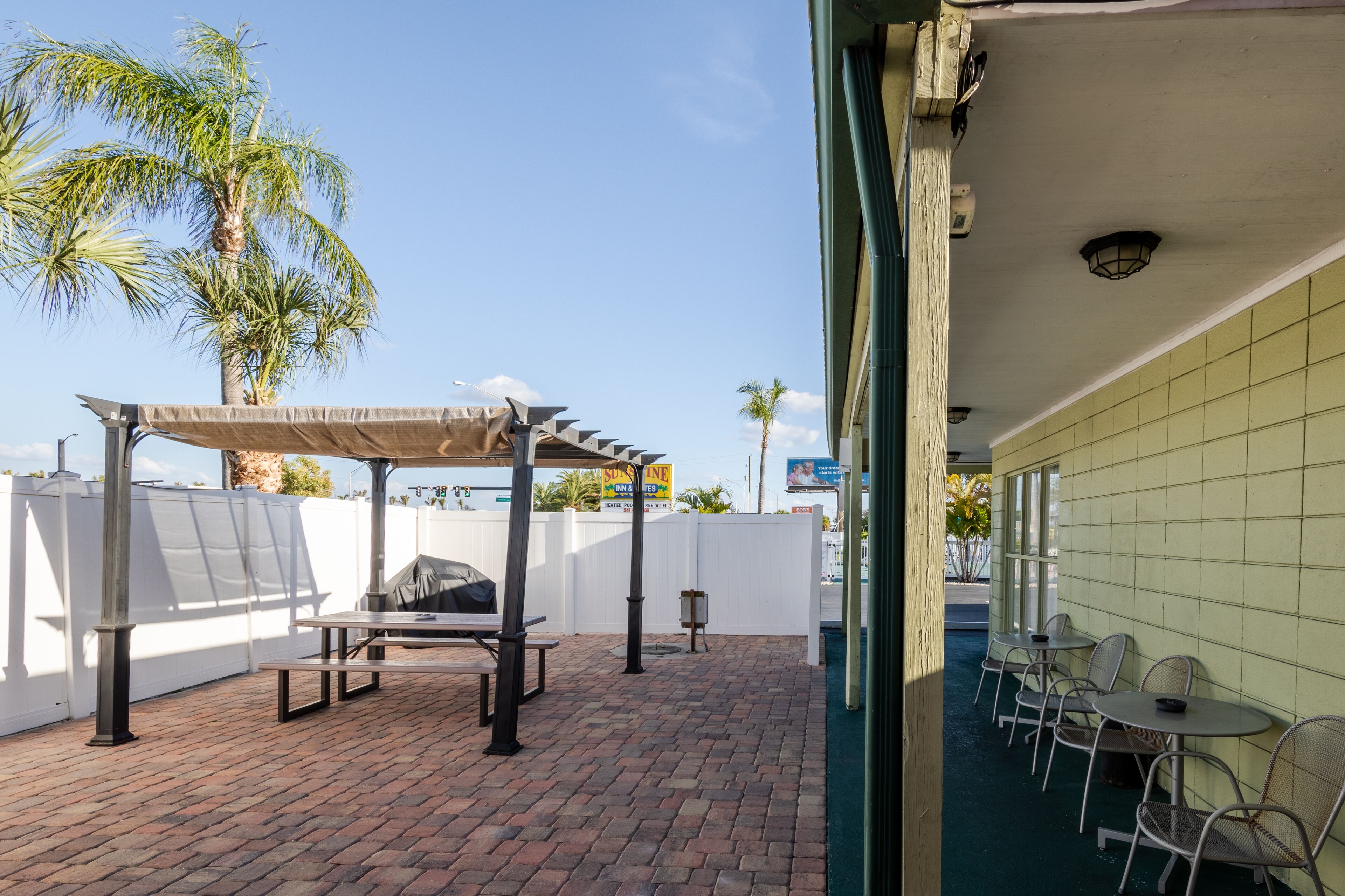 An outdoor patio with a brick floor, a covered barbecue area, and a seating area with tables and chairs.