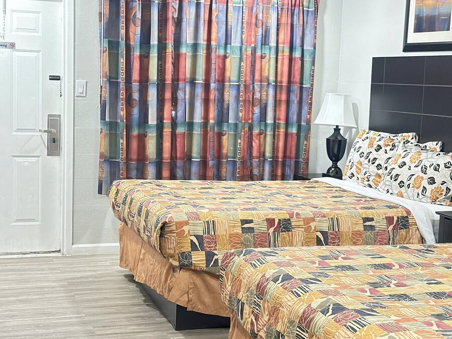 Una camera d'albergo con due letti, una ventola a soffitto, una finestra con tende a motivi e un quadro appeso al muro.