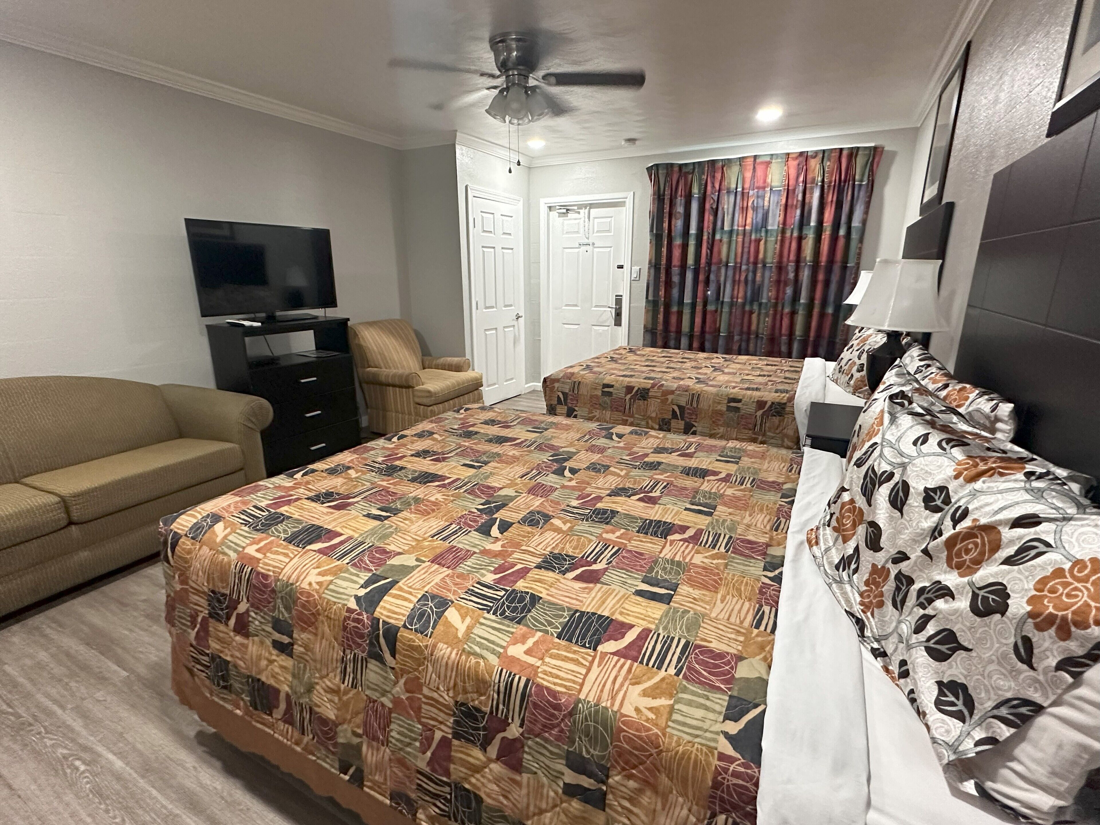 A hotel room with a large bed, a sofa, a TV, and a ceiling fan.