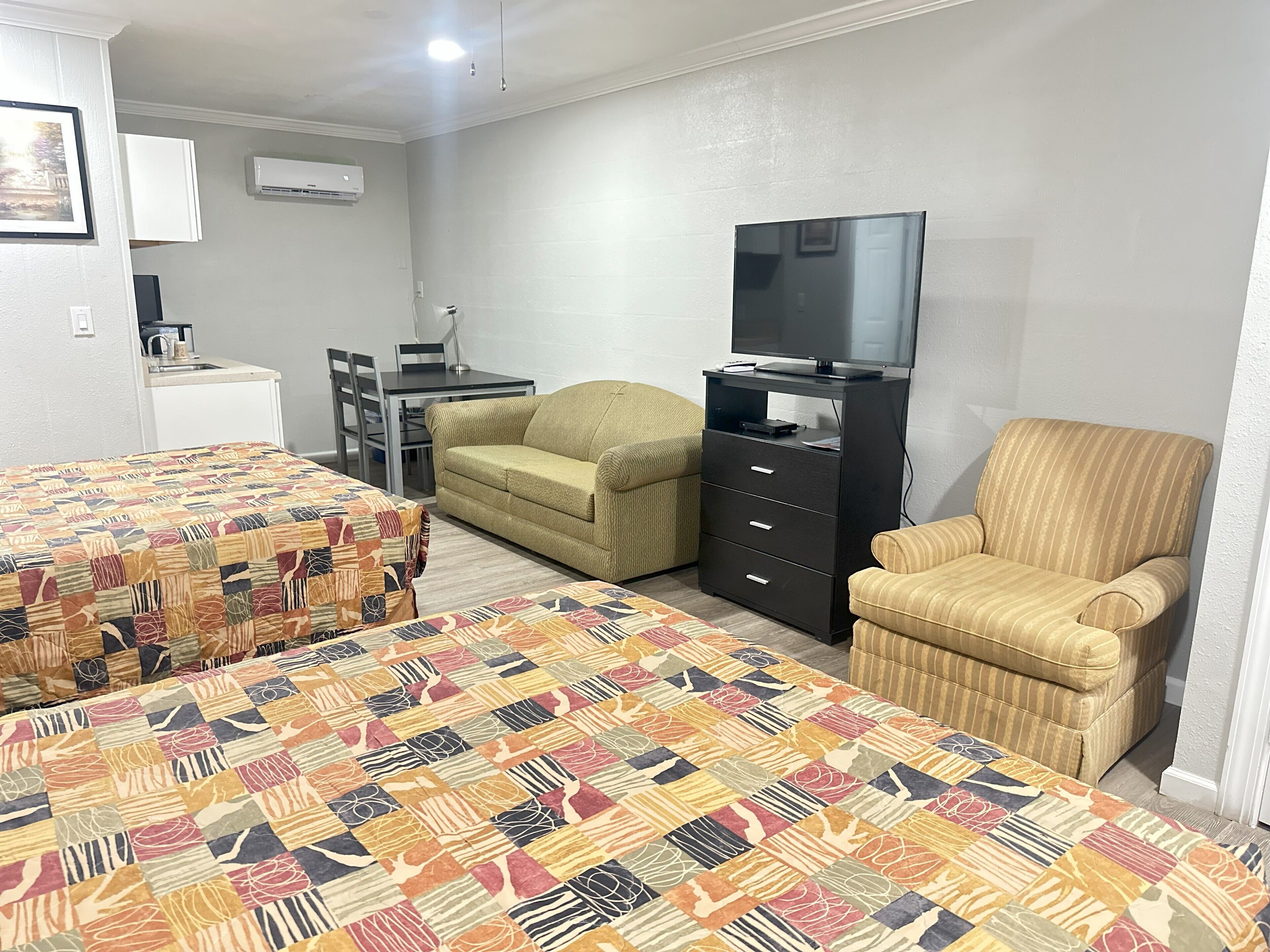 A hotel room with two beds, a sofa, a TV on a stand, a desk, and a chair.