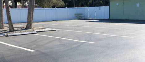 Un estacionamiento con líneas blancas que delimitan los espacios, un edificio verde y una cerca blanca.