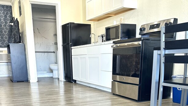 A modern kitchen with white cabinets, a stainless steel refrigerator, a microwave, and an oven. - Sunshine Inn & Suites Venice, FL (Venice)