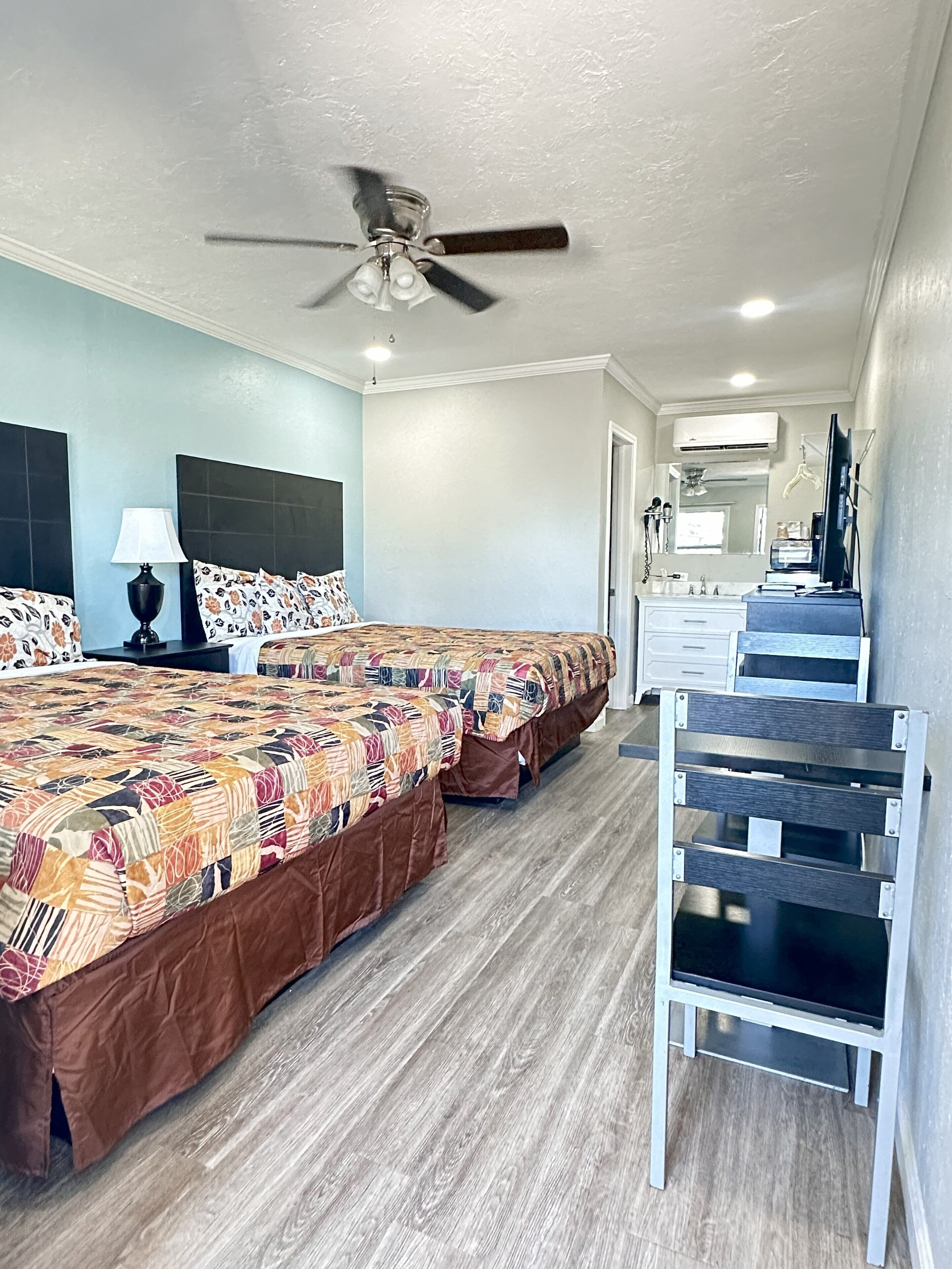 A hotel room with two beds, a ceiling fan, a desk, and a chair.