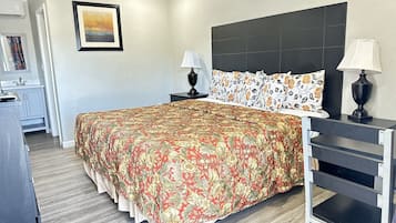 Une chambre à coucher avec un grand lit, deux tables de chevet avec des lampes, une commode, un tableau encadré au mur et un ventilateur de plafond.