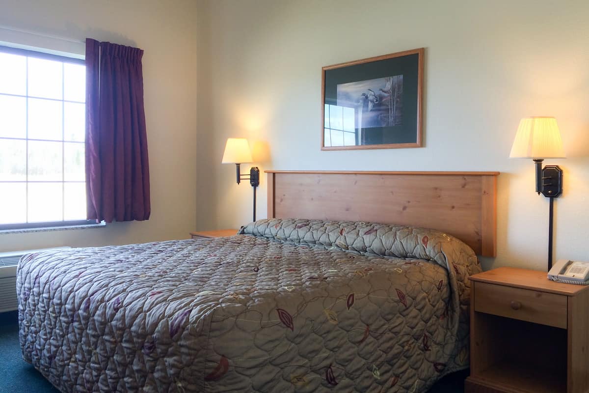 A hotel room with a large bed, two bedside lamps, a wooden nightstand, and a framed picture on the wall.