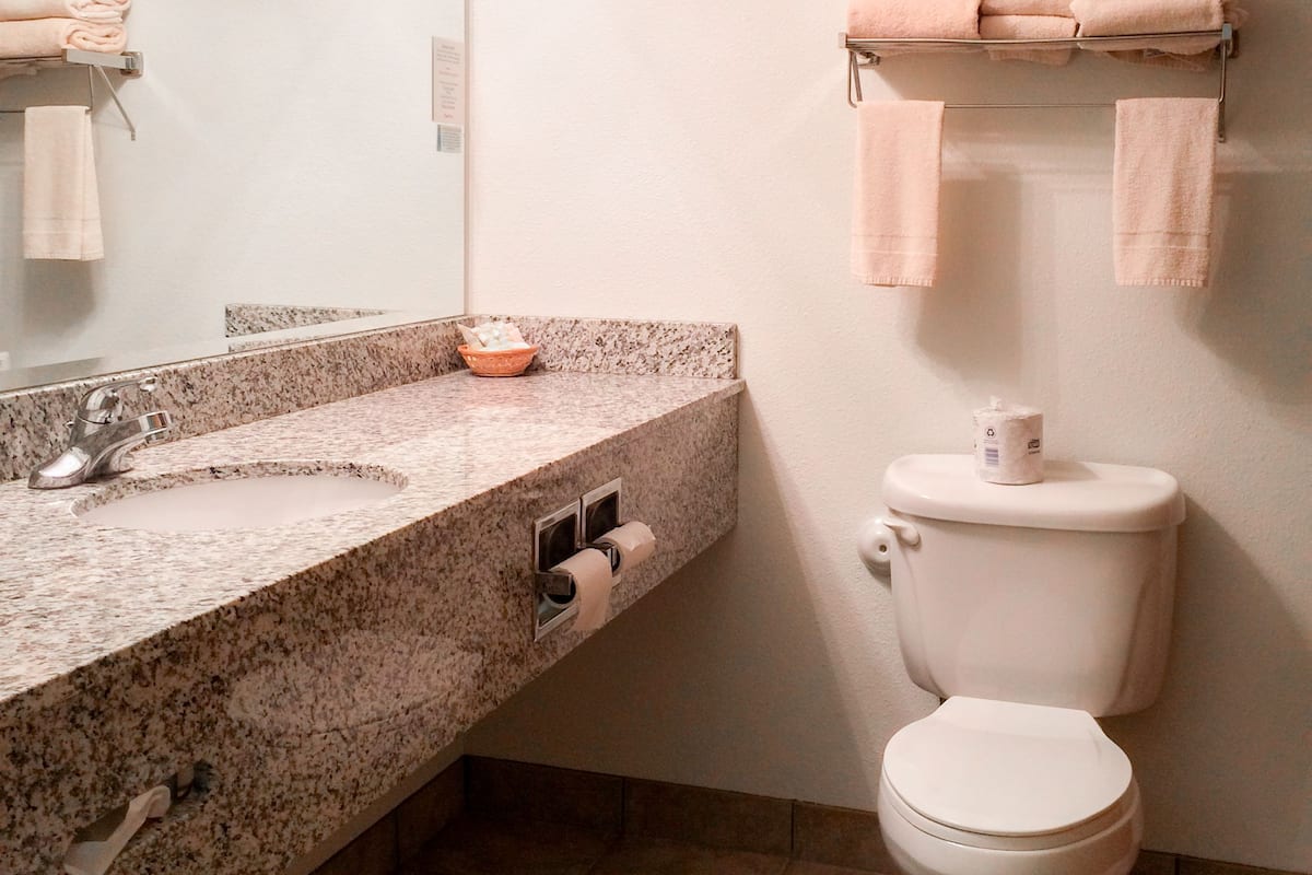 A bathroom with a granite countertop sink, a mirror, a toilet, and a towel rack with folded towels.