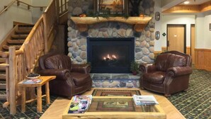 A cozy living room with a stone fireplace, leather armchairs, a coffee table with magazines, and a staircase. - White Oak Inn & Suites (Deer River)