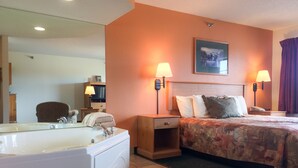 A hotel room with a large bathtub, two bedside lamps, a bed with floral bedding, and a framed picture on the wall. - White Oak Inn & Suites (Deer River)