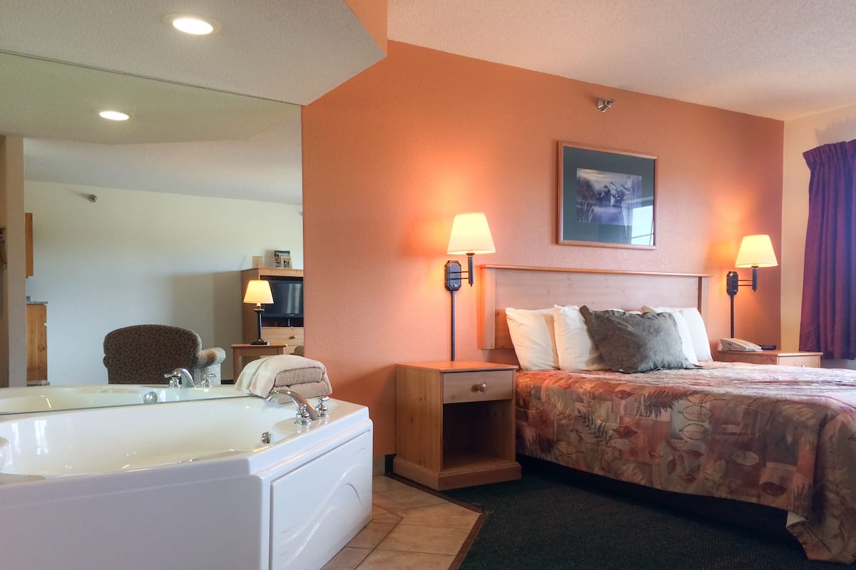 A hotel room with a large bathtub, two bedside lamps, a bed with floral bedding, and a framed picture on the wall.