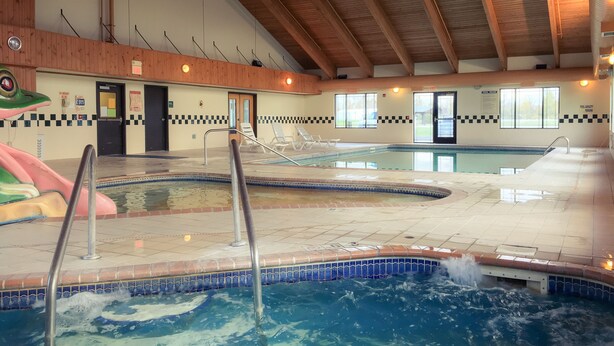 An indoor swimming pool with multiple lanes, a lifeguard chair, and a poolside area with a checkered tile border. - White Oak Inn & Suites (Deer River)