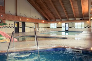 Ein Hallenbad mit mehreren Bahnen, einem Rettungsschwimmerstuhl und einem Beckenbereich mit Schachbrettmuster-Fliesenbordur.