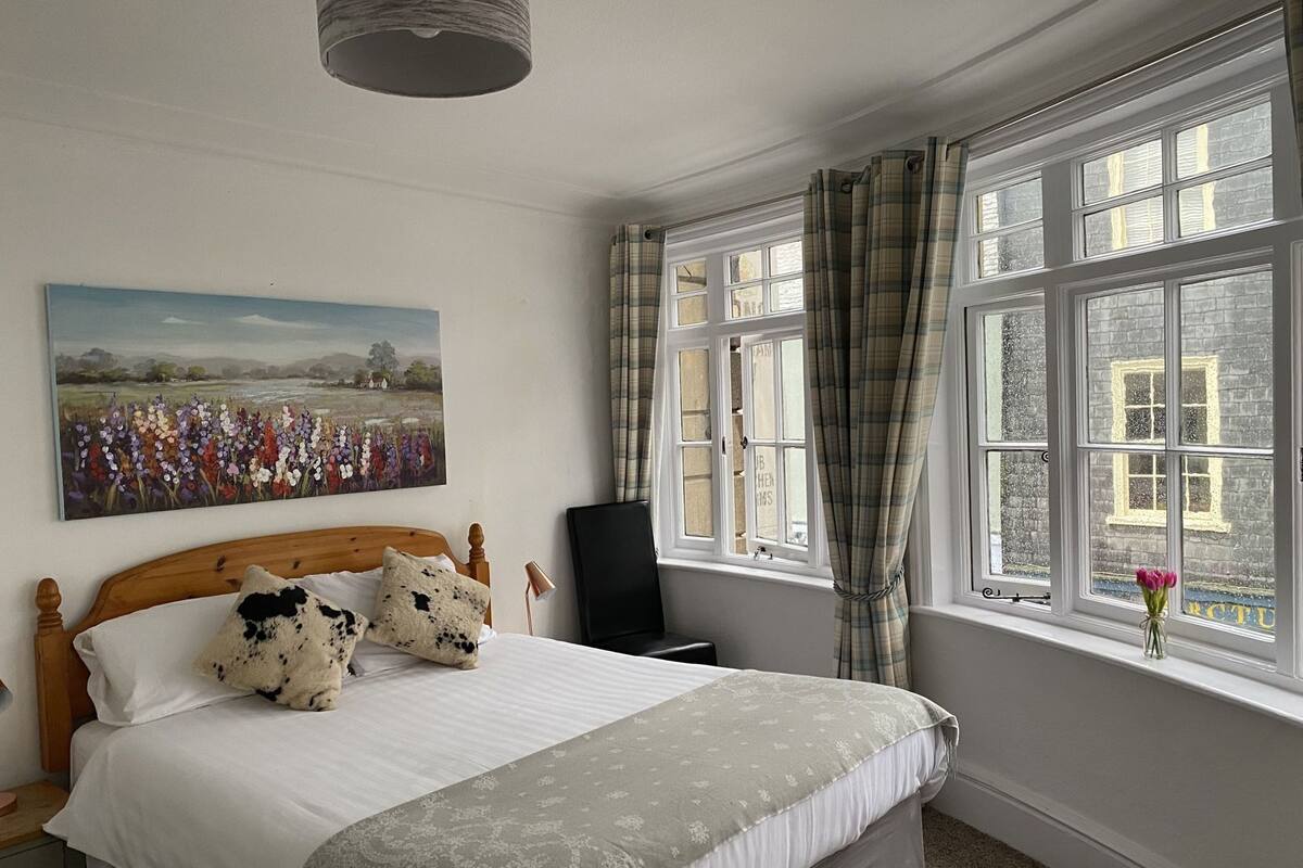 A bedroom with a bed, a painting, a window with curtains, and a chair.