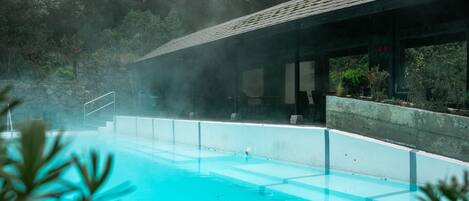 A clear blue pool with a stone wall and a covered area with benches.
