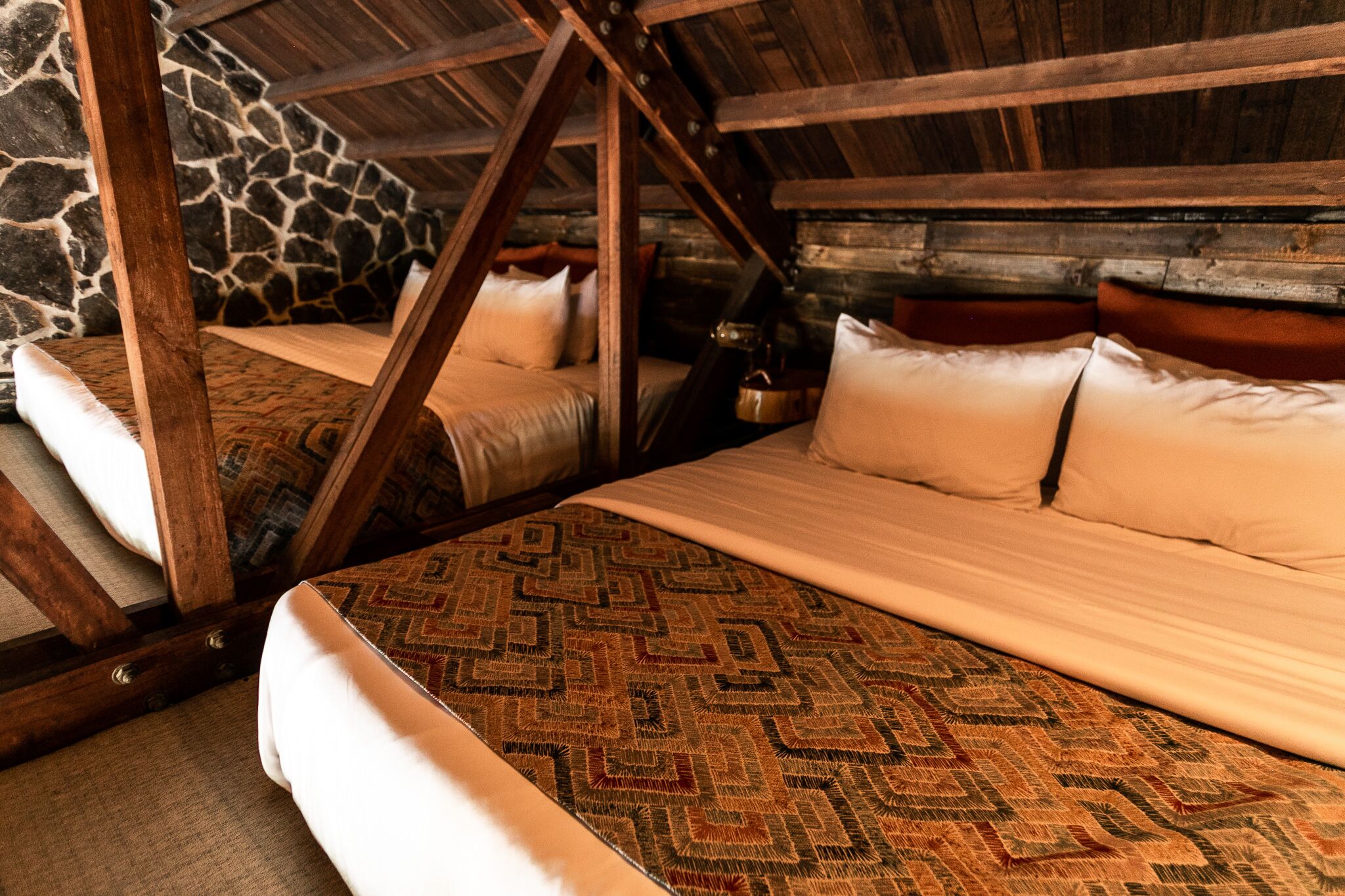 A rustic room with two beds, wooden beams, and a stone wall.