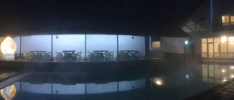 A pool area with a stone wall, outdoor seating, and a building with large windows.
