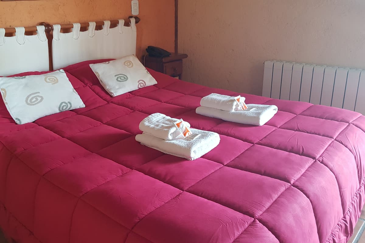 Una cama con un edredón rojo, dos almohadas y dos toallas dobladas.