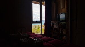 Una habitación con poca luz, una cama, un televisor y vistas al paisaje a través de una ventana.