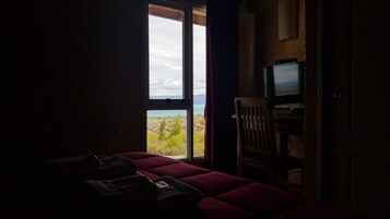 Una habitación con poca luz, una cama, un televisor y vistas al paisaje a través de una ventana.