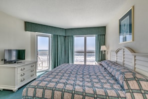 A hotel room with a large bed, a TV on a dresser, and a balcony with a view of the ocean. - Watch Resort by Condo-World (North Myrtle Beach)