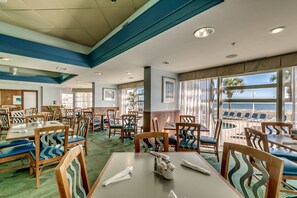 A restaurant with tables and chairs, a green carpet, and a view of the ocean.