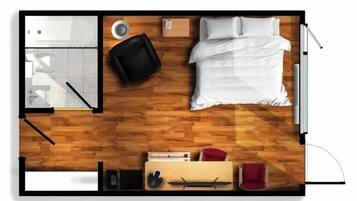 Vista cenital de una habitación de hotel con una cama, un escritorio, una silla, una mesita y un sofá.