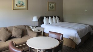 Une chambre d’hôtel avec un lit, une table de chevet avec une lampe, une chaise, une petite table et deux tableaux encadrés au mur.