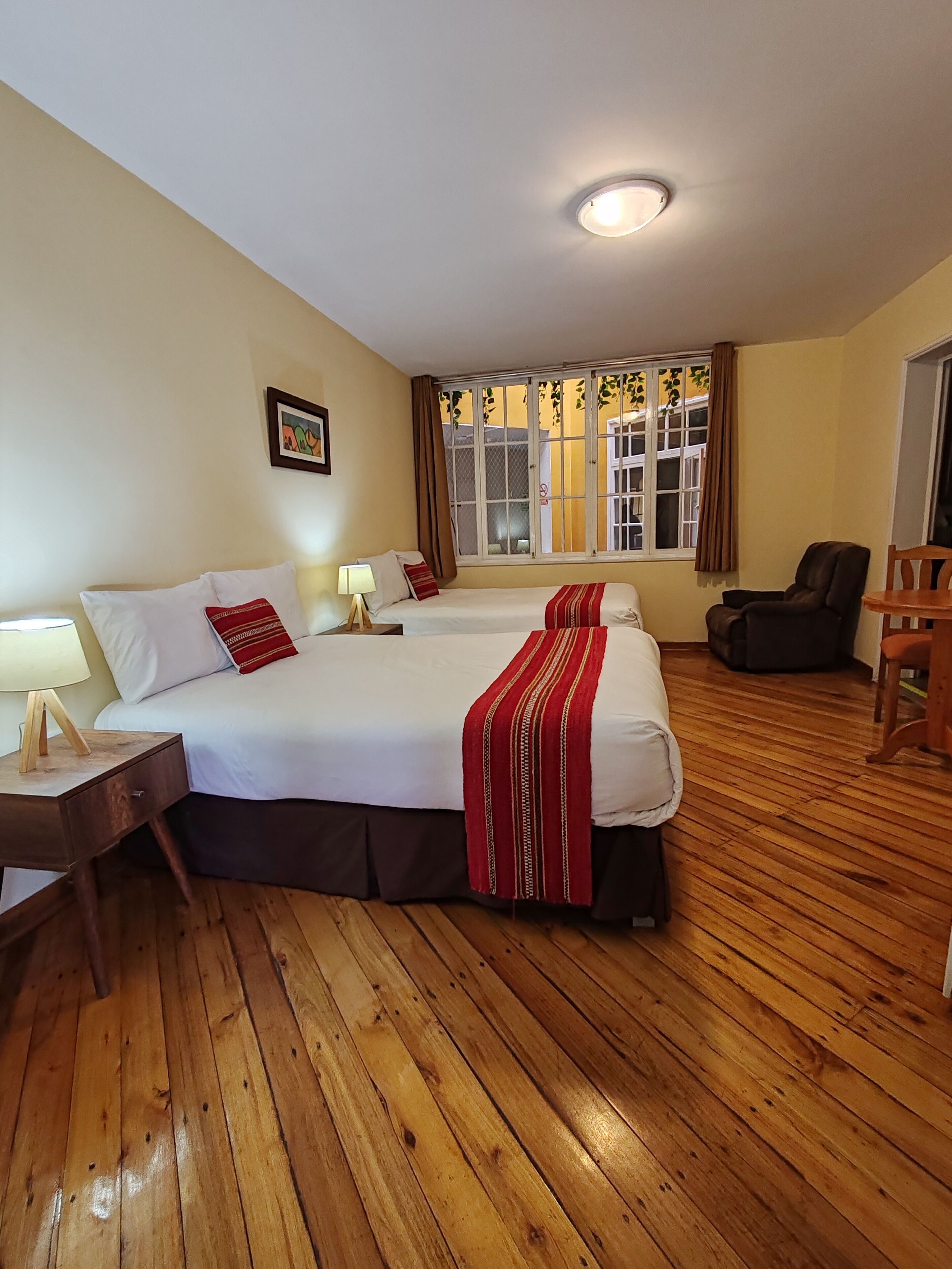 Quarto de hotel com uma cama grande, escrivaninha, cadeira e janela com cortinas.