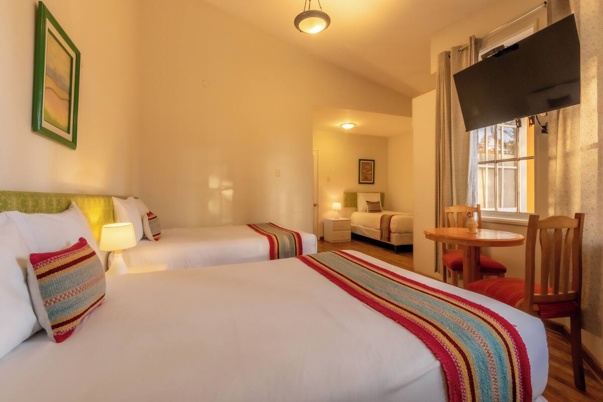 A hotel room with two beds, a TV, a small table, and a window with curtains.
