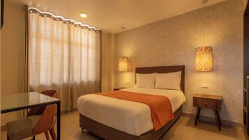 A hotel room with a bed, a bedside table, a chair, a glass table, and curtains.