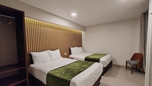 Quarto de hotel com duas camas, cabeceira de madeira, manta verde e uma cadeira.