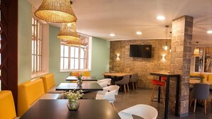 Restaurante com mesas altas, assentos acolchoados e luminárias de vime suspensas.