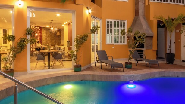 Um hotel com vários andares, área de piscina, mesas ao ar livre e plantas em vasos.