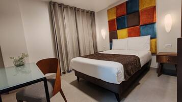 Una camera d'albergo con un letto, una scrivania, una sedia, un vaso con fiori e un pannello decorativo colorato.
