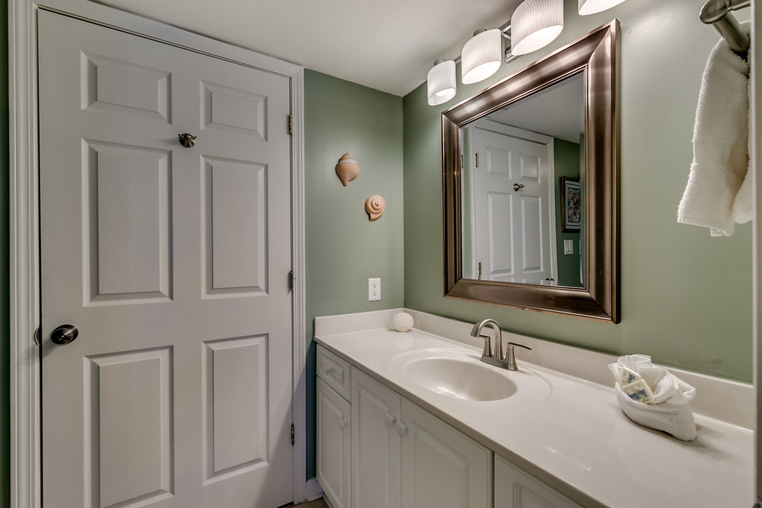 A bathroom with a white door, a sink with a mirror, and decorative shells on the wall.