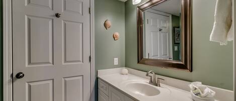 A bathroom with a white door, a sink with a mirror, and decorative shells on the wall.