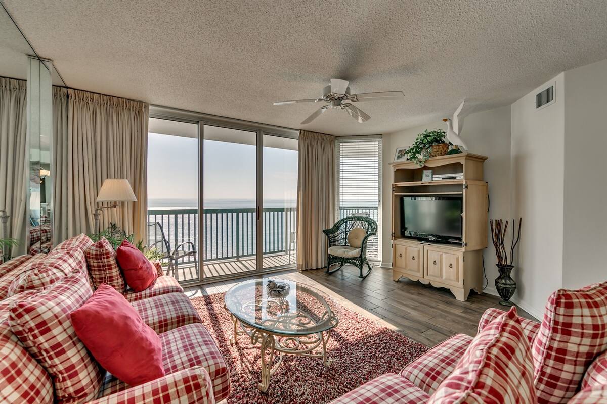 A spacious living room with a large window, a ceiling fan, a television, and a cozy seating area.